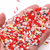 A hand holds a pile of red and white polymer clay slices assorted for DIY crafts.