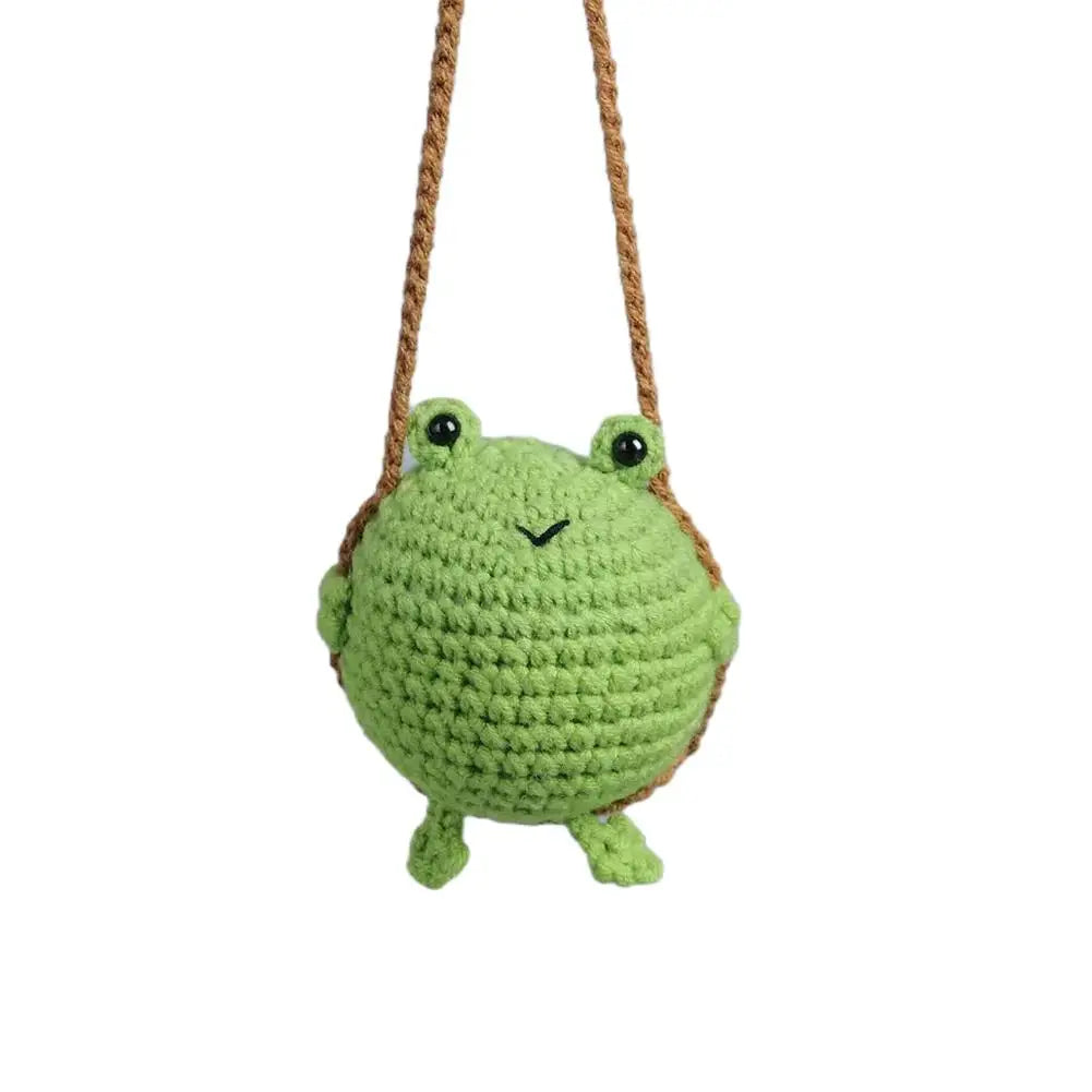 Hand-crocheted green frog with a mirror attached, hanging from a brown string.