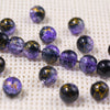 A line of purple gradient crystal glass beads with a golden crackle finish scattered on a white textured surface.