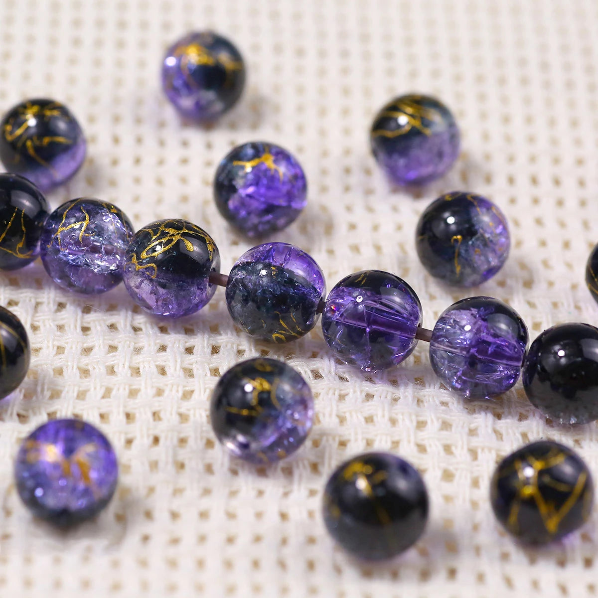 A line of purple gradient crystal glass beads with a golden crackle finish scattered on a white textured surface.