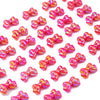A close-up of small, sparkly pink and gold acrylic bow beads scattered on a white background.