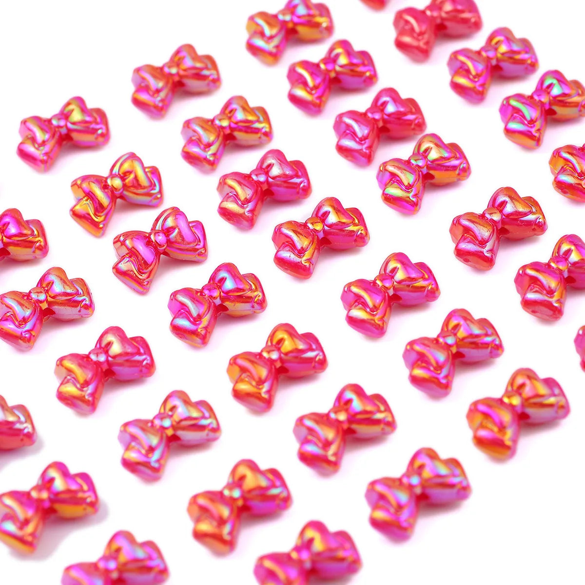 A close-up of small, sparkly pink and gold acrylic bow beads scattered on a white background.