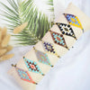 A bundle of metallic glass beads in various geometric patterns and colors is displayed on a beige fabric.
