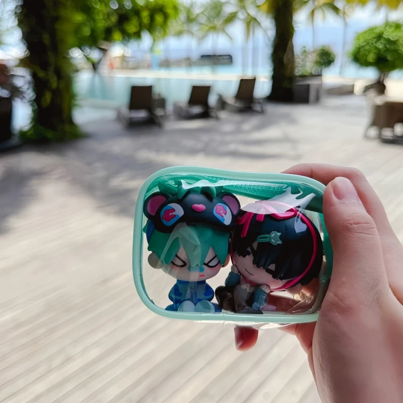 A hand holds a blind box featuring two cute anime-style figures with green and purple hair and accessories.