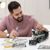 A man is assembling a 282-piece metal steam locomotive model kit on a white table with blueprints and tools.