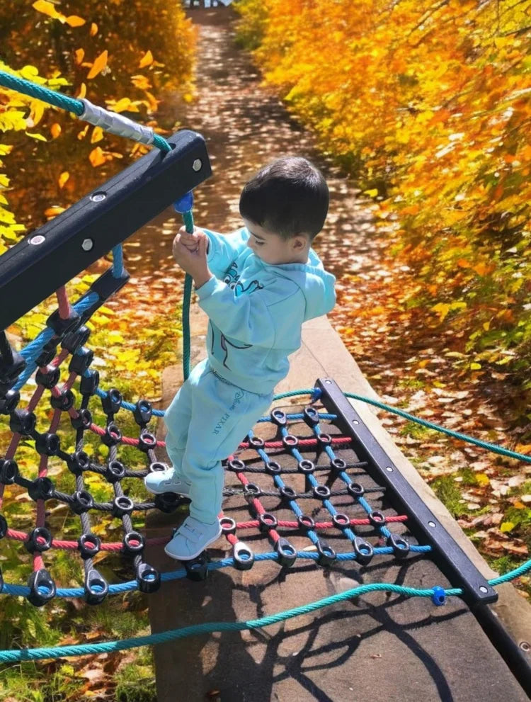 A young boy is playing on a playground structure made of black and blue hooks and loops outdoors.