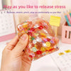 A hand holds a translucent, colorful fruit ice cube stress ball, demonstrating its squeeze and stretch features.