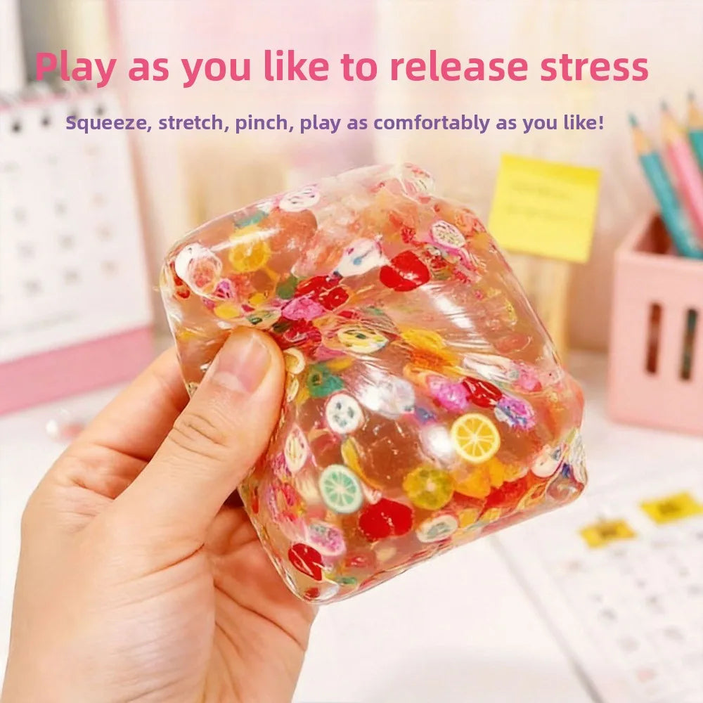 A hand holds a translucent, colorful fruit ice cube stress ball, demonstrating its squeeze and stretch features.
