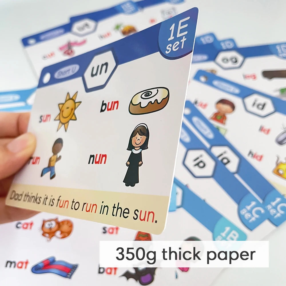 A hand holds a phonics learning card showing the word sun and an illustration of the sun.