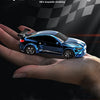 A blue 1:64 scale RC drift racing car is held in a hand against a dark, checkered background.