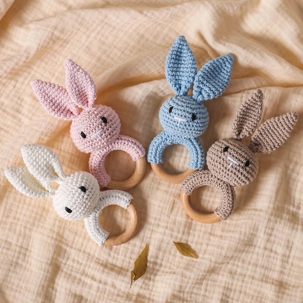 A set of handmade crochet bunny rattles in pink, blue, and cream colors resting on a light fabric.