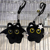 A black plush cat keychain charm with yellow eyes and a white star detail hanging from a black cord.