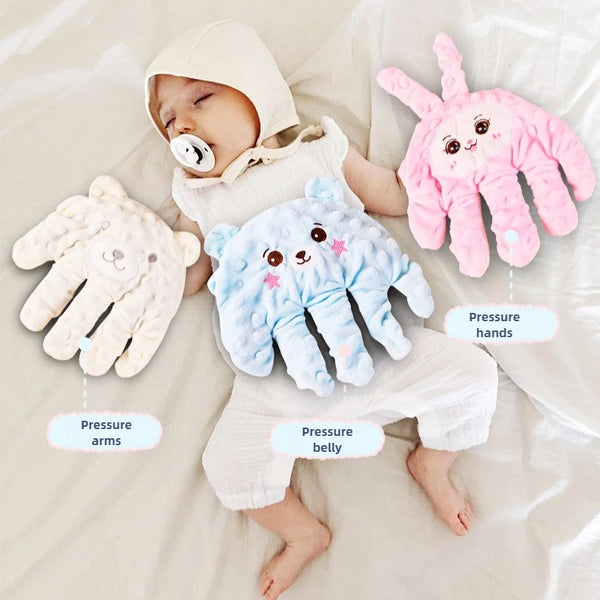 A baby is lying on a sheet surrounded by soft, pink and blue silicone hands for sensory play.