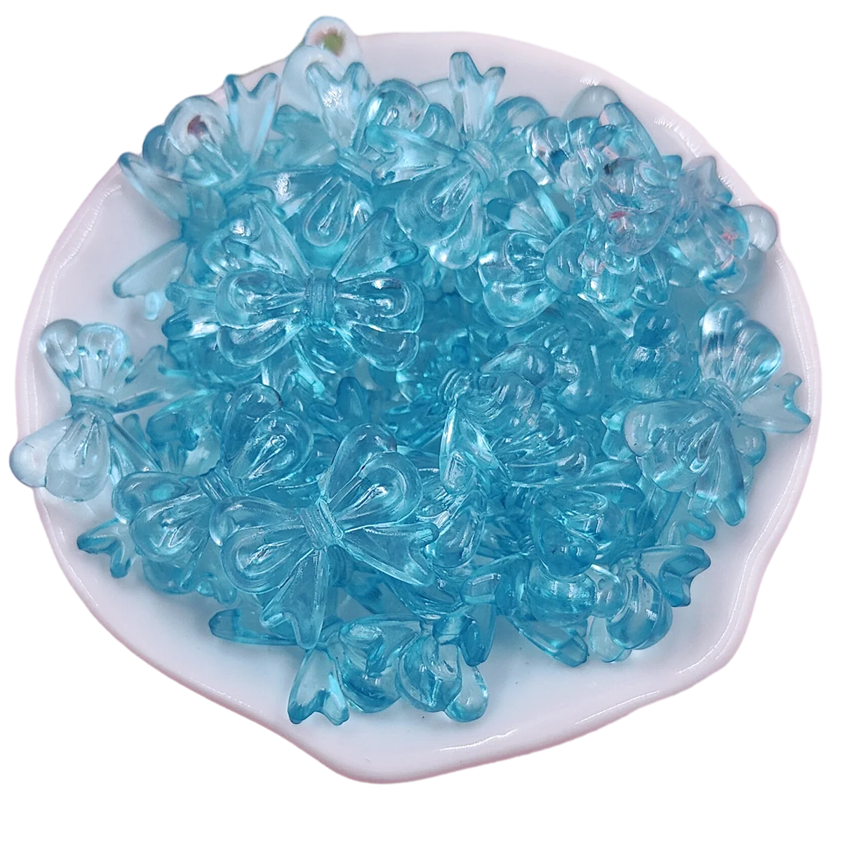 A pile of small, translucent blue acrylic bow beads for jewelry making.