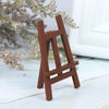 A small, rustic wooden artist easel used for dollhouses, resting on a white surface with lavender branches in the background.