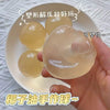 A hand holds a translucent yellow squeeze ball made from coconut oil, used for stress relief.