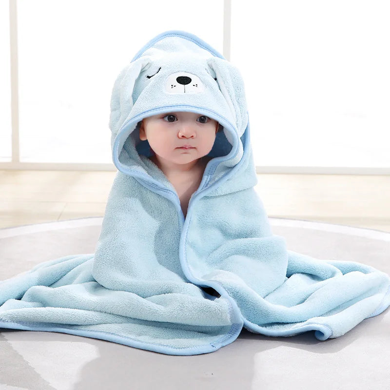 A baby wearing a light blue hooded animal bath towel with a cute face design.