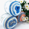 Spools of gradient rainbow cotton-wool yarn showing various shades of blue, white, orange, and green.