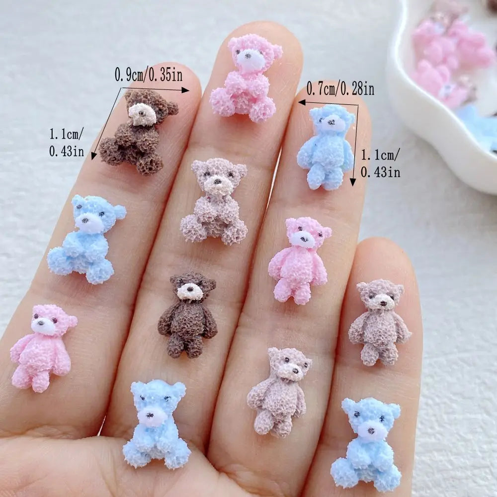 A hand displays various mini resin teddy bear charms in pink, blue, and brown colors, showing different sizes.
