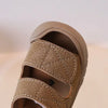 A close-up of a tan suede toddler sandal for children, showing the stitching and soft sole.