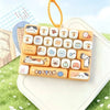 A set of 26 cartoon animal keycap charms arranged in a rectangular tray, displayed on a white surface with green grass in the