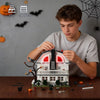 A boy is assembling a miniature haunted house model made of building blocks and accessories.