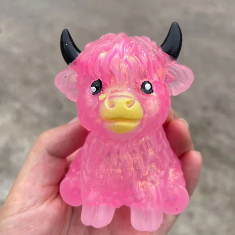 A pink glitter highland cow squishy stress relief fidget toy is held in a hand.