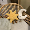 A yellow sun and white moon plushie set resting on a light-colored surface next to a wicker chair.