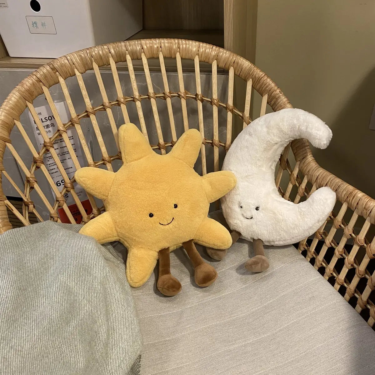 A yellow sun and white moon plushie set resting on a light-colored surface next to a wicker chair.