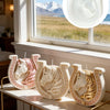 Three decorative white ceramic candle molds shaped like horses with Celtic knot designs displayed on a shelf.
