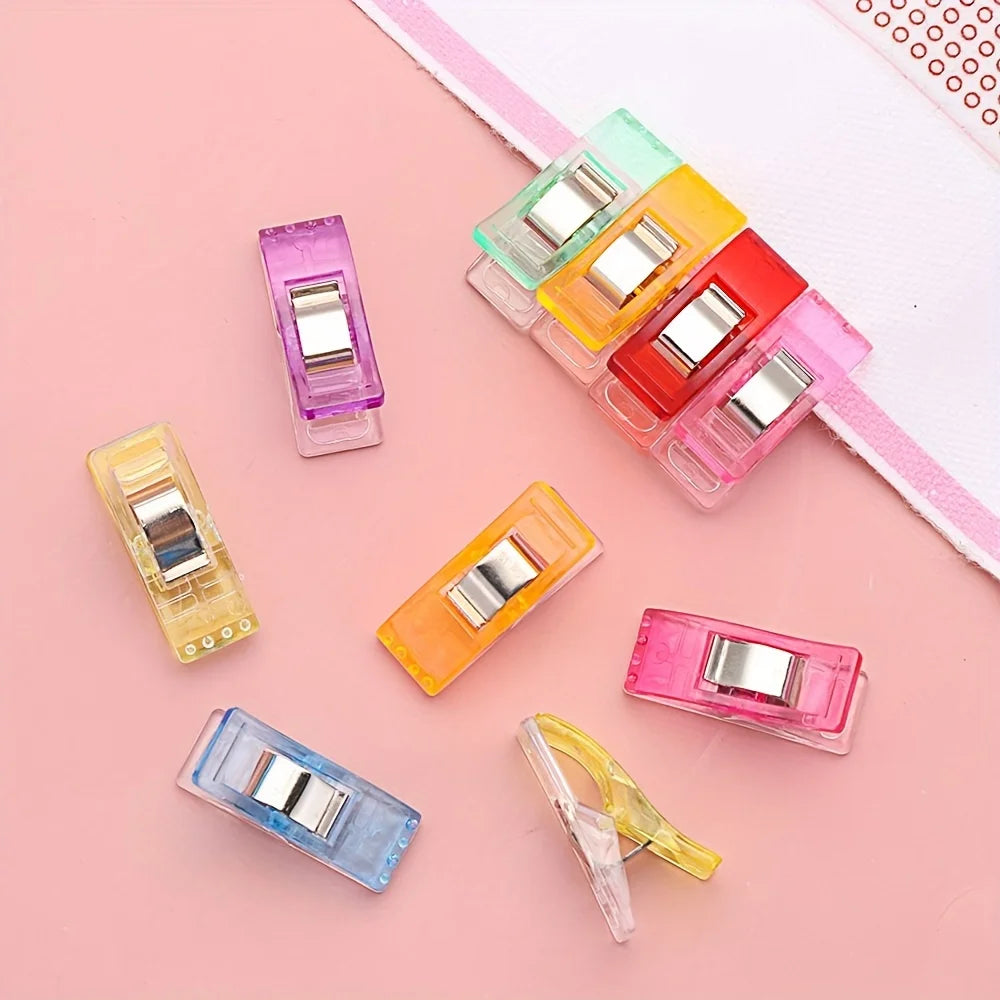 An assortment of eight plastic diamond painting clips in various colors including pink, yellow, green, and red, arranged on a