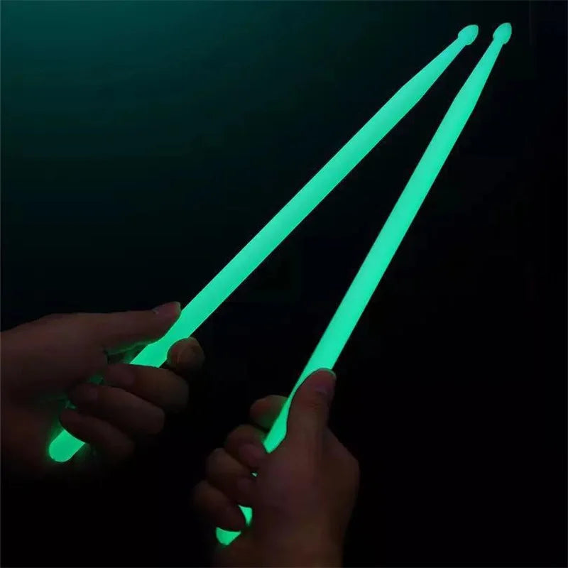 Hands holding glowing green nylon drumsticks against a dark background.