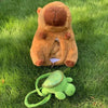 A large brown capybara plush toy with a gaping mouth revealing smaller baby capybaras, set in green grass.