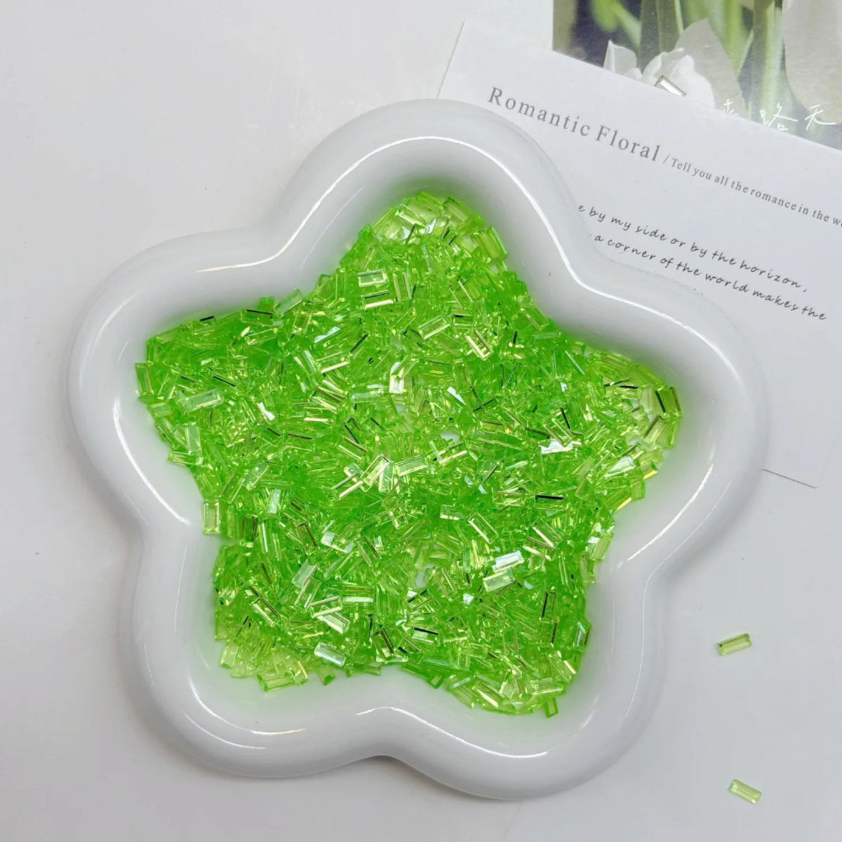 A white heart-shaped container filled with bright green acrylic ice strips for nail art and DIY crafts.