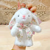 A white soft bunny plush toy with a floral bow charm is being held by a hand.