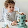 A toddler is using a green Montessori screwdriver board toy to practice fine motor skills and shape matching.