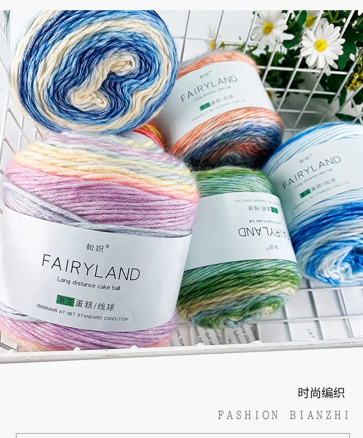 A variety of colorful gradient yarn balls in various shades of blue, pink, green, and yellow are displayed in a white crate.