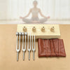 A set of silver tuning forks and wooden resonance boxes displayed on a light brown surface.