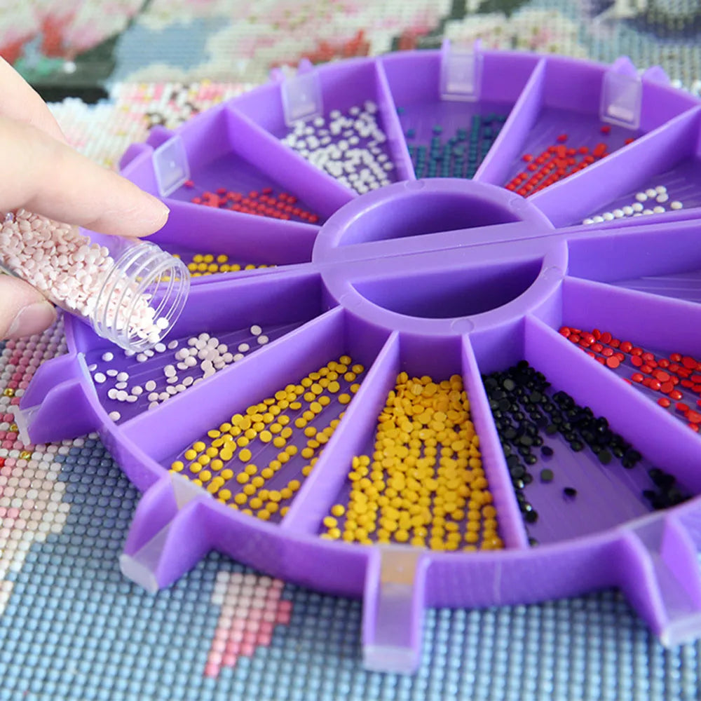 A hand is placing small colored beads into a 6-compartment diamond painting organizer tray.