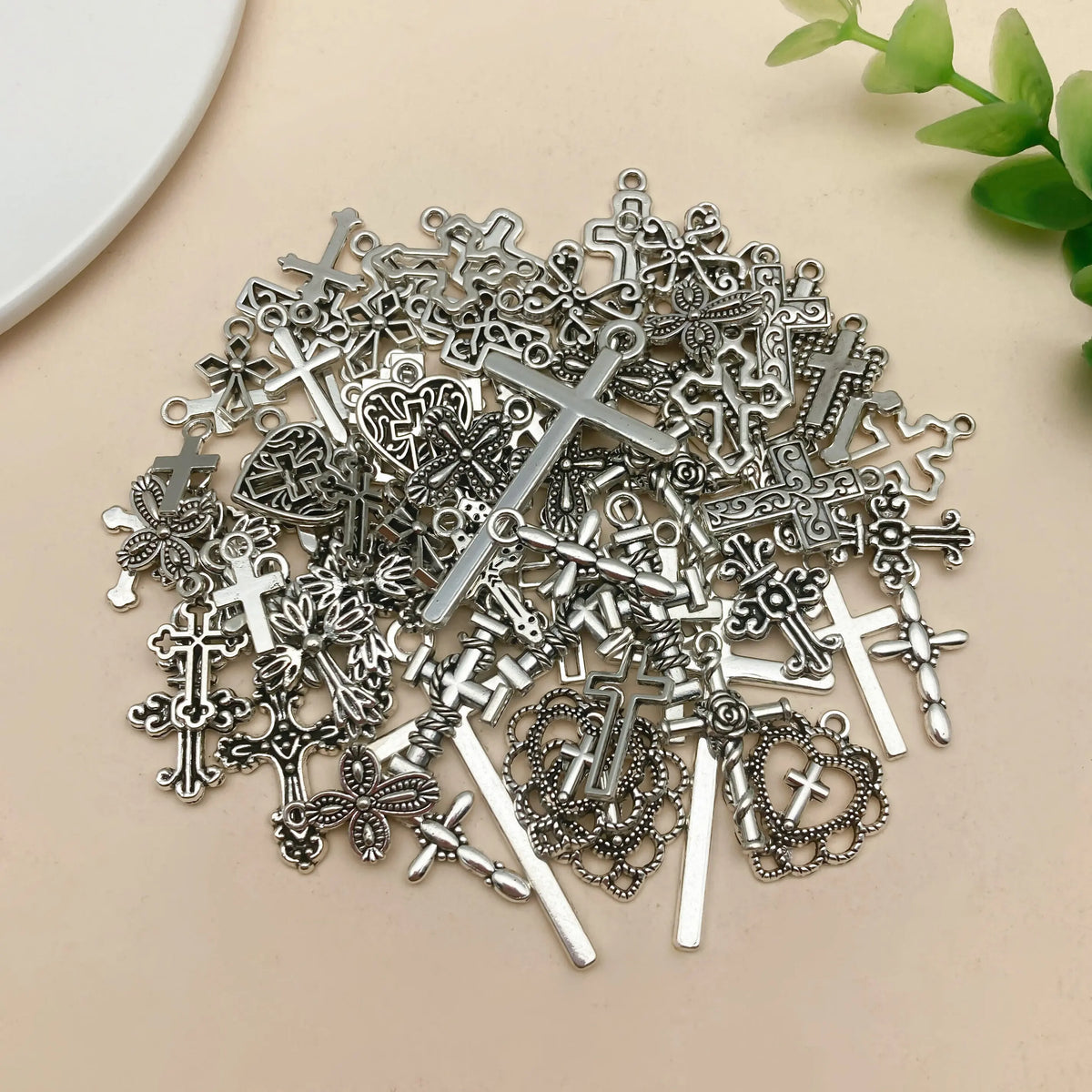 A pile of vintage silver cross charms and pendants for jewelry making scattered on a light background.