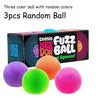 Three colorful fuzz balls in purple, green, and pink are displayed next to their packaging box.
