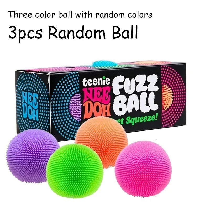 Three colorful fuzz balls in purple, green, and pink are displayed next to their packaging box.