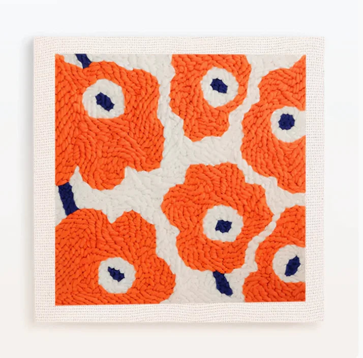 A square piece of white fabric with an orange flower pattern embroidered in orange yarn and blue accents.