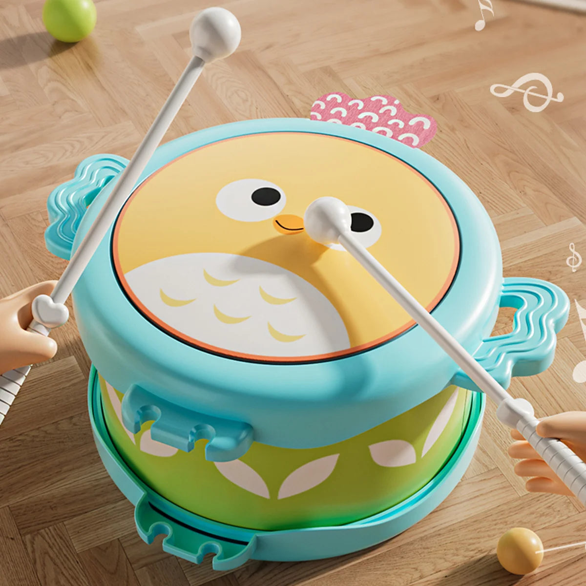 A bright blue owl double-sided musical drum for kids with yellow and white features resting on a wooden floor.