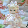 A delicate white and pink collectible figurine of a girl with large eyes and a bow, set against a soft floral background.