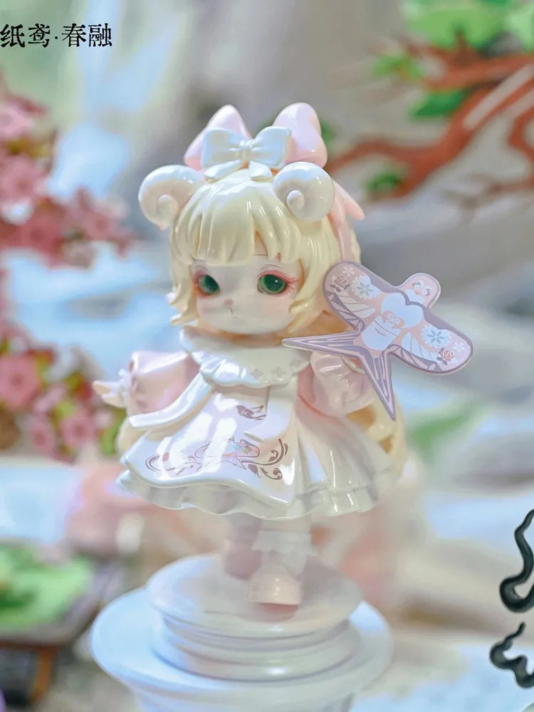 A delicate white and pink collectible figurine of a girl with large eyes and a bow, set against a soft floral background.