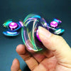 A hand holds a colorful metal fidget spinner, showing its iridescent and reflective surface.