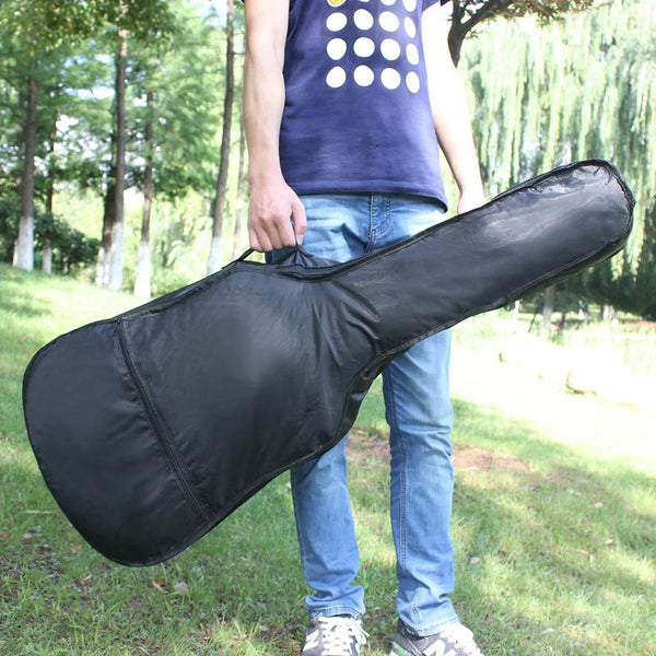 A person holds a black portable acoustic guitar carrying bag outdoors.