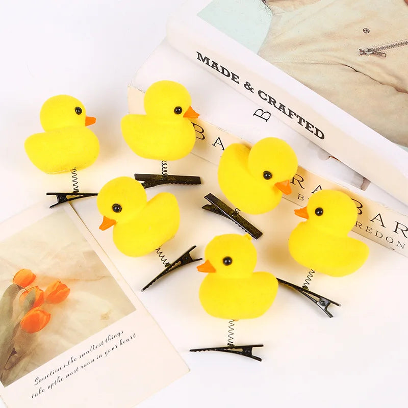 A collection of bright yellow 3D duck plush hair clips displayed on a white background next to an open book.