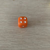 A single orange acrylic die with five white dots is placed on a light wooden surface.